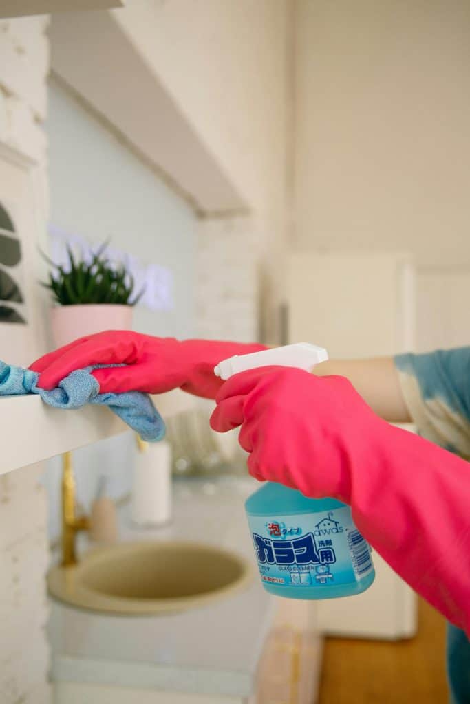Clendo cleaner's hand with pink gloves is spraying eco-friendly multipurpose cleaner to clean shelves easily with a microfibre cloth.