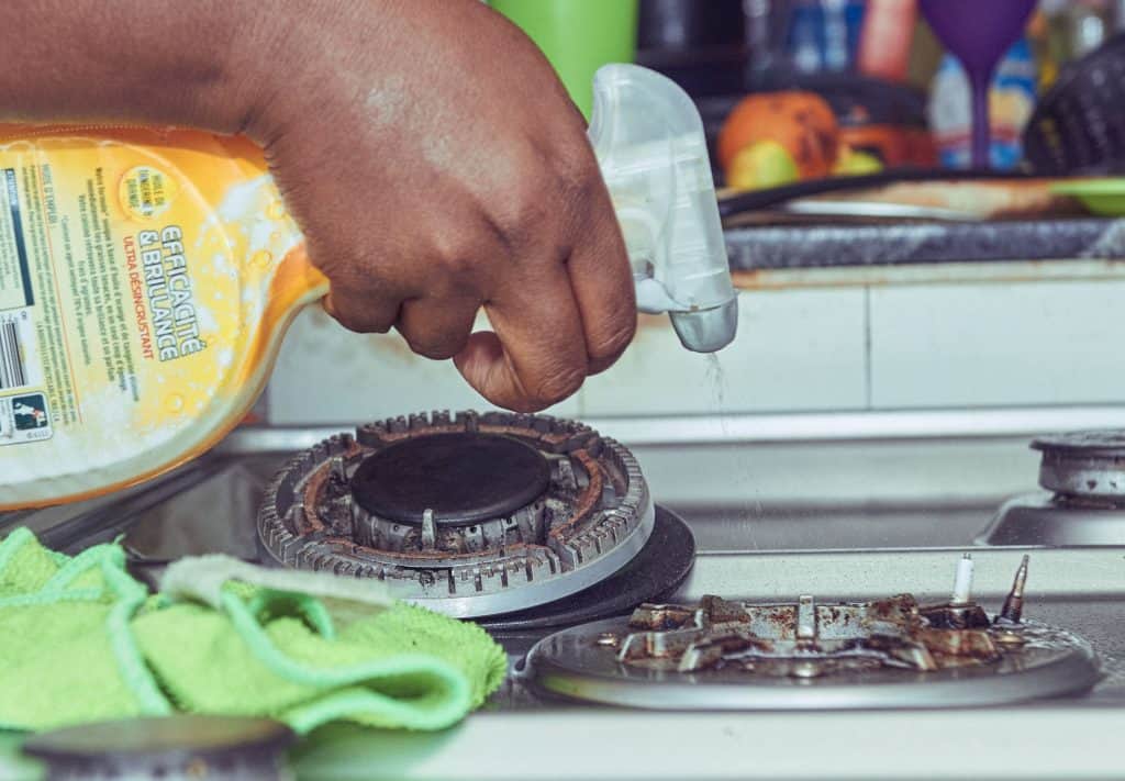 Clendo cleaner's hand spraying gas cooktop with degreaser to prepare it for cleaning
