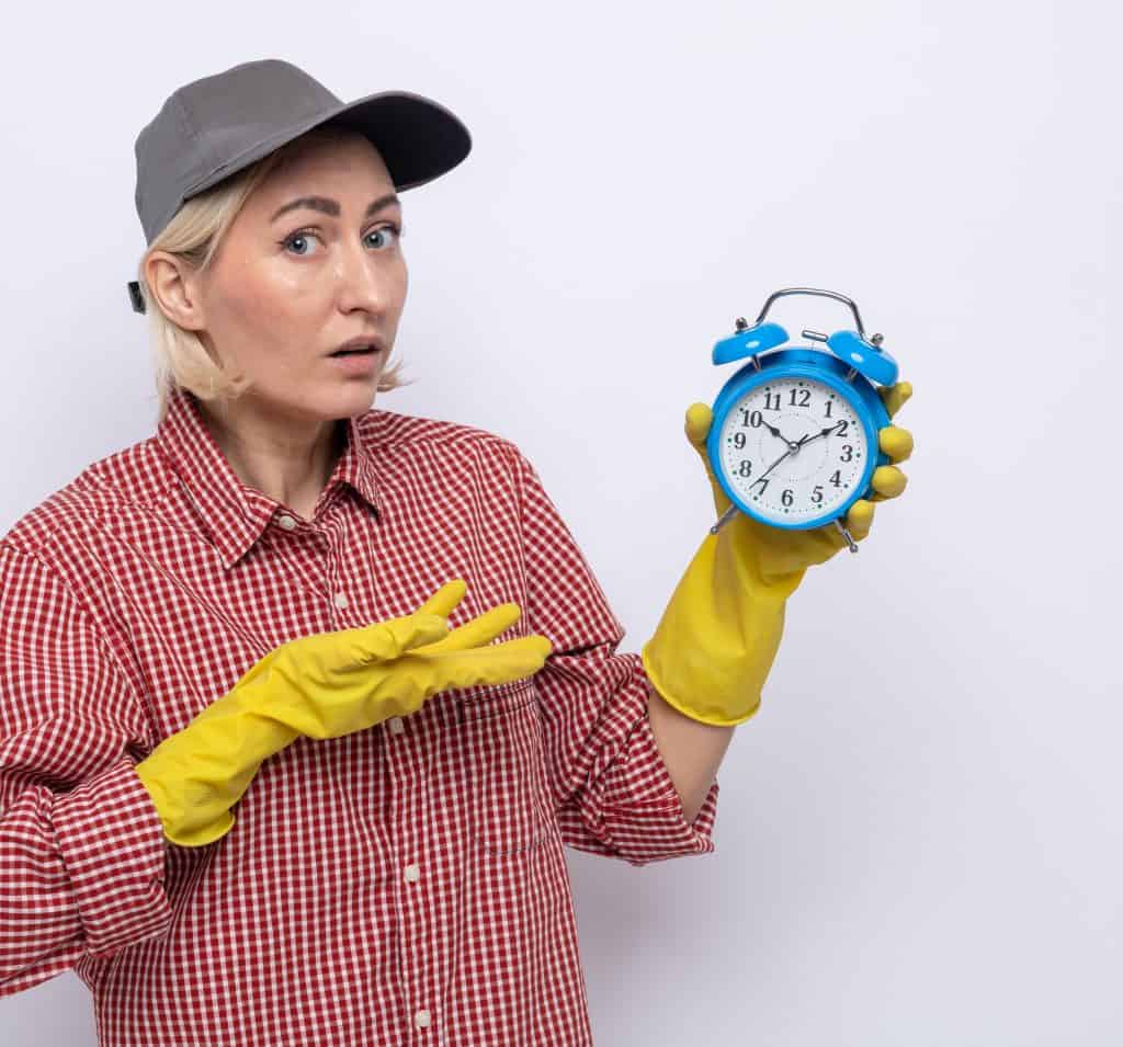 Clendo employee with yellow gloves and a cap is holding blue alarm clock signifying same day cleaning availability